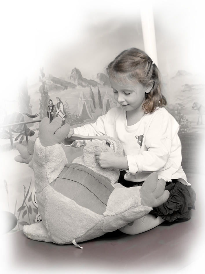 Spielendes Kind Kleines Mädchen spielt mit einem Stofftierdrachen. Sie putzt ihm mit einer riesigen Zahnbürste die Zähne.