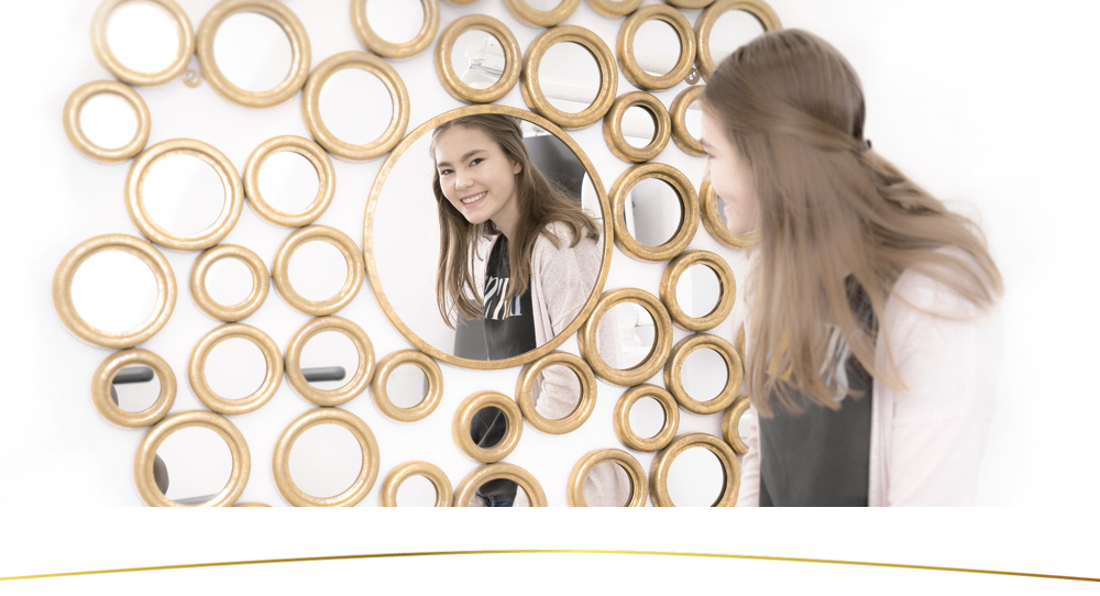 Blick in den Spiegel eine Teenagerin lächelt in einen goldenen runden Spiegel in der Zahnarztpraxis